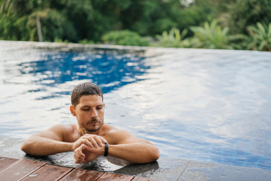 An attractive sporty man in an outdoor pool looks at the smartwatch tracker after an active swim.