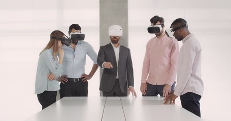 Team of young multiethnic office workers using glasses of virtual reality during business meeting in conference room. Group of employees in VR glasses. Concept of work, technology. - Powered by Adobe