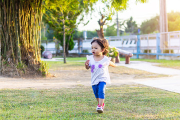 Happy Asian baby girl running and playing at the park or garden field. She smiling and laughing. Child aged 1-2 years old. Relaxation and exercise for health. Development of kid concept.