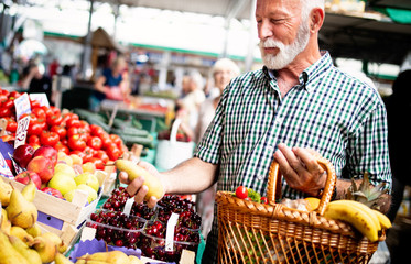 Positive elderly man buying seasonal vegetables in local market