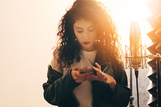 Pretty female singer in music studio with smart phone