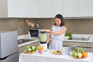 Pretty young Asian woman making smoothie in blender in the kitchen