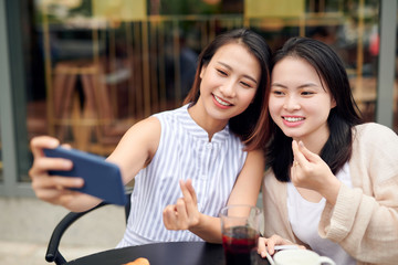Portrait of two women smiling at smartphone camera while taking selfie photo in outdoor cafe