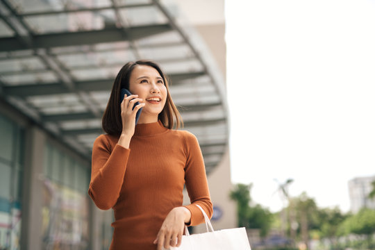 Portrait Of Happy Young Asian Woman Talking On Mobile And Carrying Paper Shopping Bags Walking Outdoor Mall