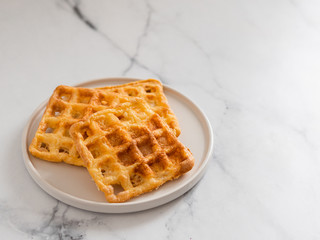 Delicious savory keto waffles. Two ingredients chaffles on plate over white marble background. Eggs and parmesan cheese low carb waffles. Copy space for text or design.