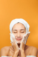 Beautiful model applying cosmetic cream treatment on her face on orange background