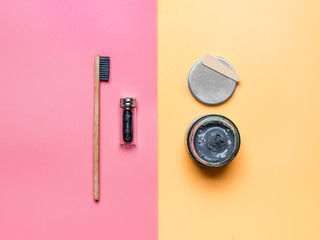 Zero waste dental care concept. Bamboo charcoal toothbrush, natural charcoal dental floss and natural charcoal toothpaste in glass on pink and yellow background - obrazy, fototapety, plakaty