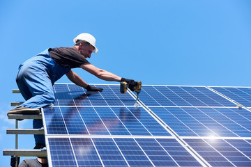 Man mounting modern solar batteries on house's roof. Using high ladder and professional drill. Environment friendly, green energy. Ecological. Using natural renewable energy. Wearing work uniform.
