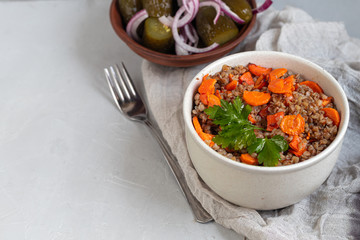 Buckwheat porridge in a bowl with stewed carrots. Decorated with green leaves. On a cotton napkin, on a light gray .