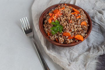 Buckwheat porridge in a bowl with stewed carrots. Decorated with green leaves. On a cotton napkin, on a light gray .