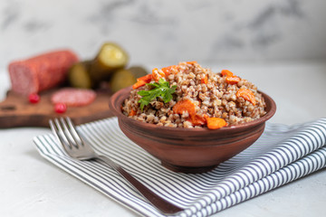 Buckwheat porridge in a bowl with stewed carrots. Decorated with green leaves. On a cotton napkin, on a light gray .