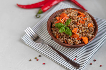 Buckwheat porridge in a bowl with stewed carrots. Decorated with green leaves. On a cotton napkin, on a light gray .