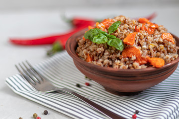 Buckwheat porridge in a bowl with stewed carrots. Decorated with green leaves. On a cotton napkin, on a light gray .