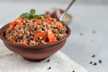 Buckwheat porridge in a bowl with stewed carrots. Decorated with green leaves. On a cotton napkin, on a light gray .