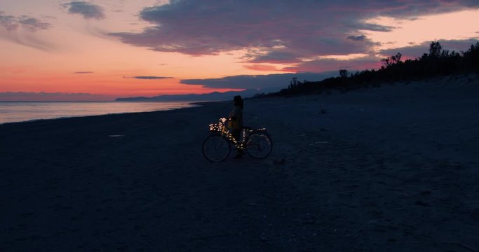 Ragazza va in giro in bicicletta di notte sulla spiaggia. Striscia illuminata di luci led.