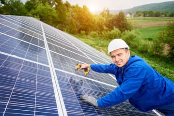 Construction worker connects photo voltaic panel to solar system using screwdriver. Professional installing and construction of solar system, looking to the camera. Alternative energy concept
