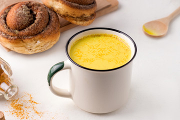 preparing indian drink golden milk on a white background. nearby spiced spices and breakfast roll