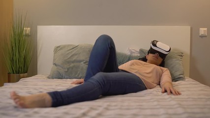 Excited young woman watching adult video in vr headset, relaxing on bed alone