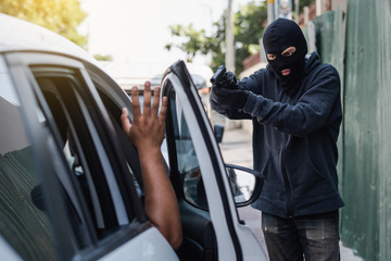 A thief  is trying to steal a car, holding a pointed gun in a car driver, hijacking