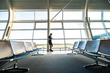 Fototapeta premium Young man waiting for departure at the airport while using his phone
