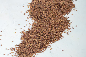 Buckwheat groats are scattered on a light background. Dark texture and background.