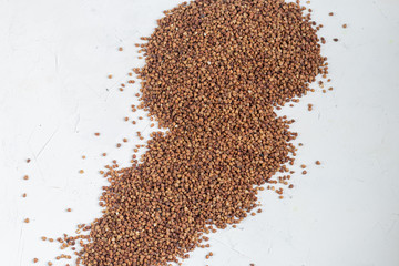 Buckwheat groats are scattered on a light background. Dark texture and background.