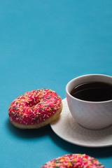 A cup of americano with two pink donuts on a blue background