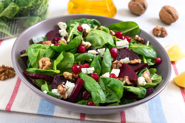 Salad with young spinach, boiled beets, blue cheese, nuts, cranberries in a bowl on a light background. Tasty diet fitness dish. Vitamin salad. Proper nutrition