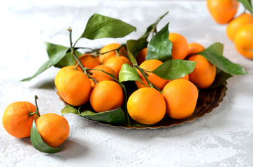 Fresh mandarin oranges fruit or tangerines with leaves in an iron tray on a gray background