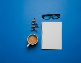  Flat composition inspired by the color of the year 2020 (classic blue) white paper, coffee with milk in cup, fir leaves, black see glasses, on bright background,