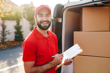Image of smiling delivery man holding clipboard and writing - Powered by Adobe
