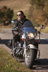 Handsome bearded motorcyclist in black leather jacket and sunglasses sitting on cruiser motorcycle...