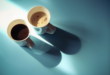 Two cups of coffee , black coffee and cappucino coffee with morning sunlight