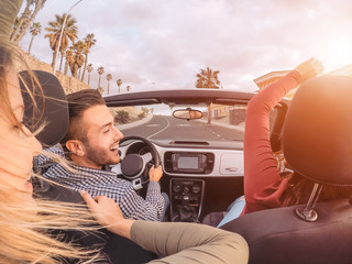 Happy friends having fun on convertible car during road trip - Group trendy young people enjoying...