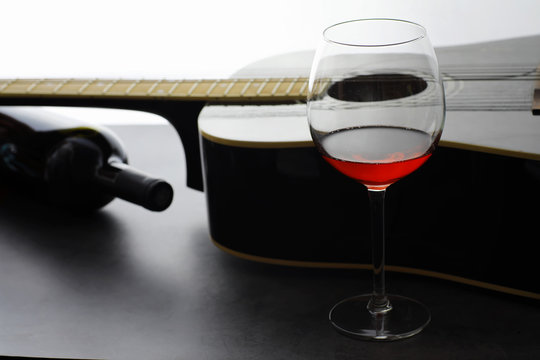 Guitar and high glass with red wine on a stone background.