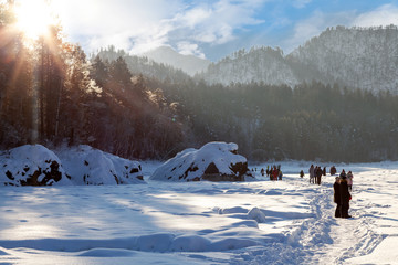 Winter landscape with people walking on a frozen river or lake in the Altai mountains on a sunny day under a blue sky with snowdrifts around.