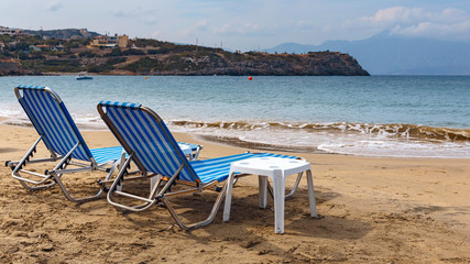 Fototapeta na wymiar two sun loungers on the sandy beach of the Greek resort town of Agios Nikolaos