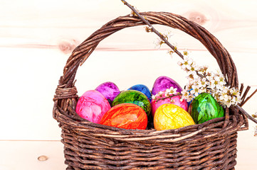 Hand-painted easter eggs in rainbow colors in a basket on a wooden background, decorated with cherry blossom. Springtime holidays concept