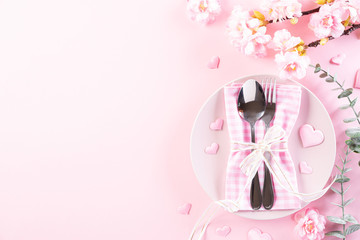 Pink paper hearts with table set with set of silverware fork and spoon on Light pink pastel paper background. Love and Valentine's day concept.