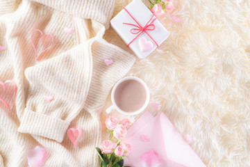 Pink paper hearts with gift box and roses, coffee cup on , beige sweater on cream colour knitted blanket and fluffy background. Love and Valentine's day during Winter concept.
