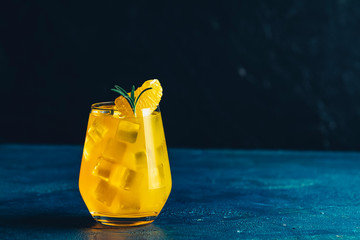 Yellow orange cocktail with tangerine and rosemary with ice in glass on dark blue concrete...