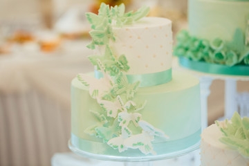Obraz na płótnie Canvas Beautiful wedding cake. The combination of white and turquoise. Decorated with beautiful butterflies. Wedding cake on restaurant interior background. Sweet cake on a festive buffet. 