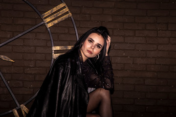 brunette in a black leather jacket on a background of a brown brick wall and a clock