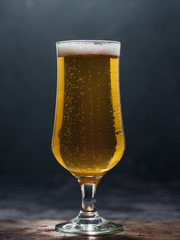 A glass of cold light beer lager on a dark background