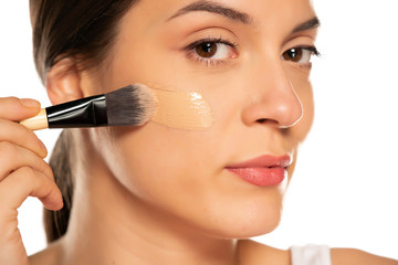 Young woman applying liquid foundation with the brush in her face