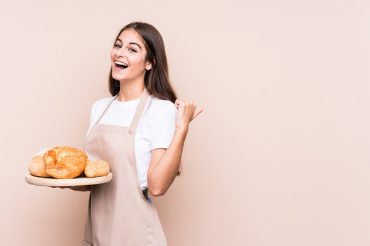 Young caucasian baker woman isolated points with thumb finger away, laughing and carefree.