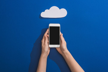 cropped view of woman holding smartphone near empty white paper cloud on blue