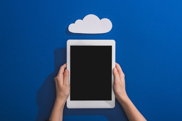 cropped view of woman holding digital tablet near empty white paper cloud on blue
