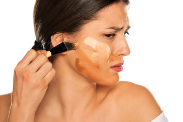 Young nervous woman smearing three different tones of liquid foundation on her face on white...