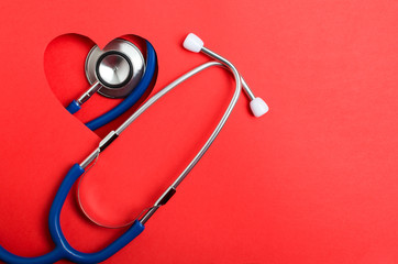 Top view of blue stethoscope and heart shape, red background. Empty space for text